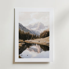 Mountain Lake Reflection Poster by Bozetto är ett kvadratiskt fototryck av en lugn bergsscen med en reflekterande sjö och tallar, med två små figurer, på FSC-certifierat premiumpapper med en lyxigt matt yta, mot en vit bakgrund.