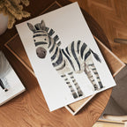 The no-9 paper, featuring a watercolor zebra illustration, rests on a wooden table beside a tray, a book, and a vase of dried flowers, creating a cozy, softly lit scene.
