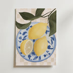 Bozetto Lemon Table Poster visar två hela citroner och en citronhalva på en blåvit blommig tallrik med gröna blad mot en beige rutig bakgrund, elegant tryckt på premium art paper.