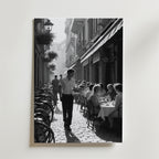 Charming Street Café Poster från Bozetto visar en svartvit scen av ett livligt utomhuscafé med gäster, en servitör och cyklar på en kullerstensgata - perfekt att visa på premiumpapper.