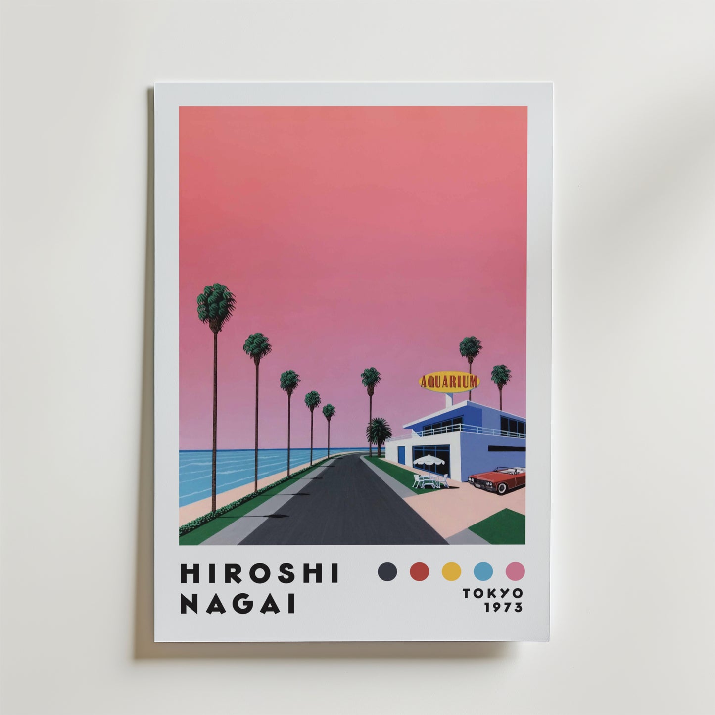Bozetto Hiroshi Nagai Sunset Coast Poster föreställer en rosa solnedgång över en palmkantad kustväg som leder till en akvariebyggnad, med "Hiroshi Nagai Tokyo 1973" och färgade prickar längst ner.