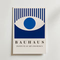 Bauhaus Blue Eye Poster från Bozetto visar ett blått och vitt abstrakt öga ovanför "BAUHAUS INSTITUTE OF ART AND DESIGN" i feta, moderna typsnitt på en ljus bakgrund, tryckt på premiumpapper med en lyxig matt finish.