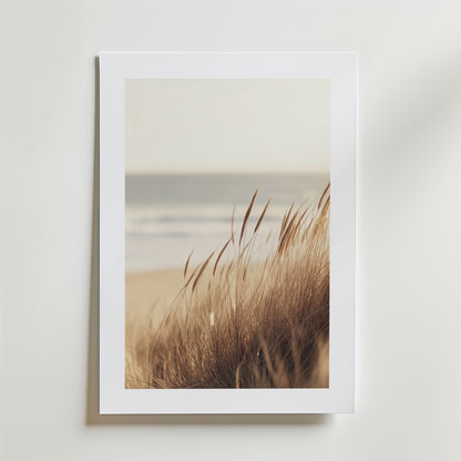 Dune Grass by the Sea Poster" av Bozetto föreställer högt, gyllene gräs på sanddyner med ett suddigt hav och himmel. Postern är tryckt på FSC-certifierat premiumpapper och de mjuka, dämpade tonerna framkallar en lugn och fridfull stämning.