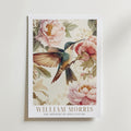 The Hummingbird Garden William Morris Poster by Bozetto visar en illustrerad kolibri bland rosa pioner och gröna blad, vilket framkallar vintage botanisk charm. Texten lyder: WILLIAM MORRIS: THE ARTISTRY OF 19TH CENTURY.
