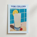 Bozetto's Tom Collins Cocktail Poster visar ett högt glas med citron, is och körsbär på en blå kaklad bakgrund. Receptet visas i fet text ovanför, allt tryckt på premiumpapper för en elegant look.