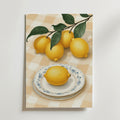 På Lemon Picnic No.2 Poster by Bozetto syns fem ljusgula citroner - en på en dekorativ tallrik, fyra på en bladgren - på en beige- och vitrutig duk. Tryckt på premiumpapper och FSC-certifierat för hållbarhet.