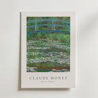 Bozetto Claude Monet Footbridge Poster visar The Japanese Footbridge med en grön bågbro över en damm med rosa näckrosor, frodig grönska och har Monets namn och konstverkets titel nedan på premiumpapper.