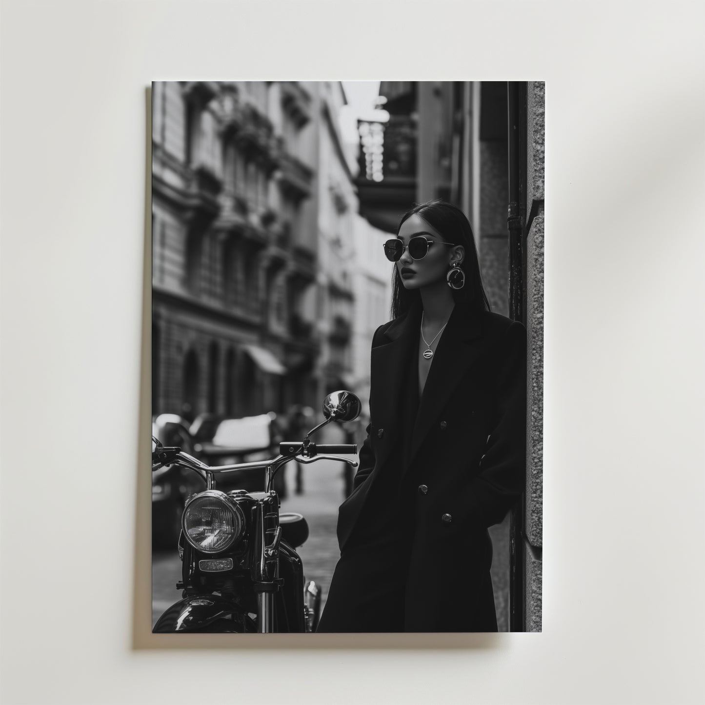 Noire Elegance Fashion Poster från Bozetto visar en elegant kvinna i lång rock och solglasögon som lutar sig på en motorcykel mot stadens skyskrapor. Den svartvita designen erbjuder en högkvalitativ finish för tidlös elegans.