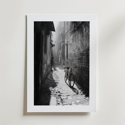 Quiet Echo Poster by Bozetto har ett svartvitt foto av en smal kullerstensgränd där solljuset kastar en cykels skugga genom dimman, tryckt på FSC-certifierat premiumpapper för en högkvalitativ finish.