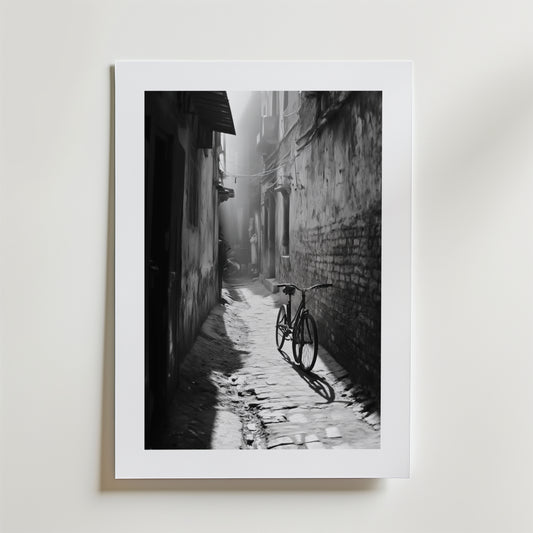 Quiet Echo Poster by Bozetto har ett svartvitt foto av en smal kullerstensgränd där solljuset kastar en cykels skugga genom dimman, tryckt på FSC-certifierat premiumpapper för en högkvalitativ finish.