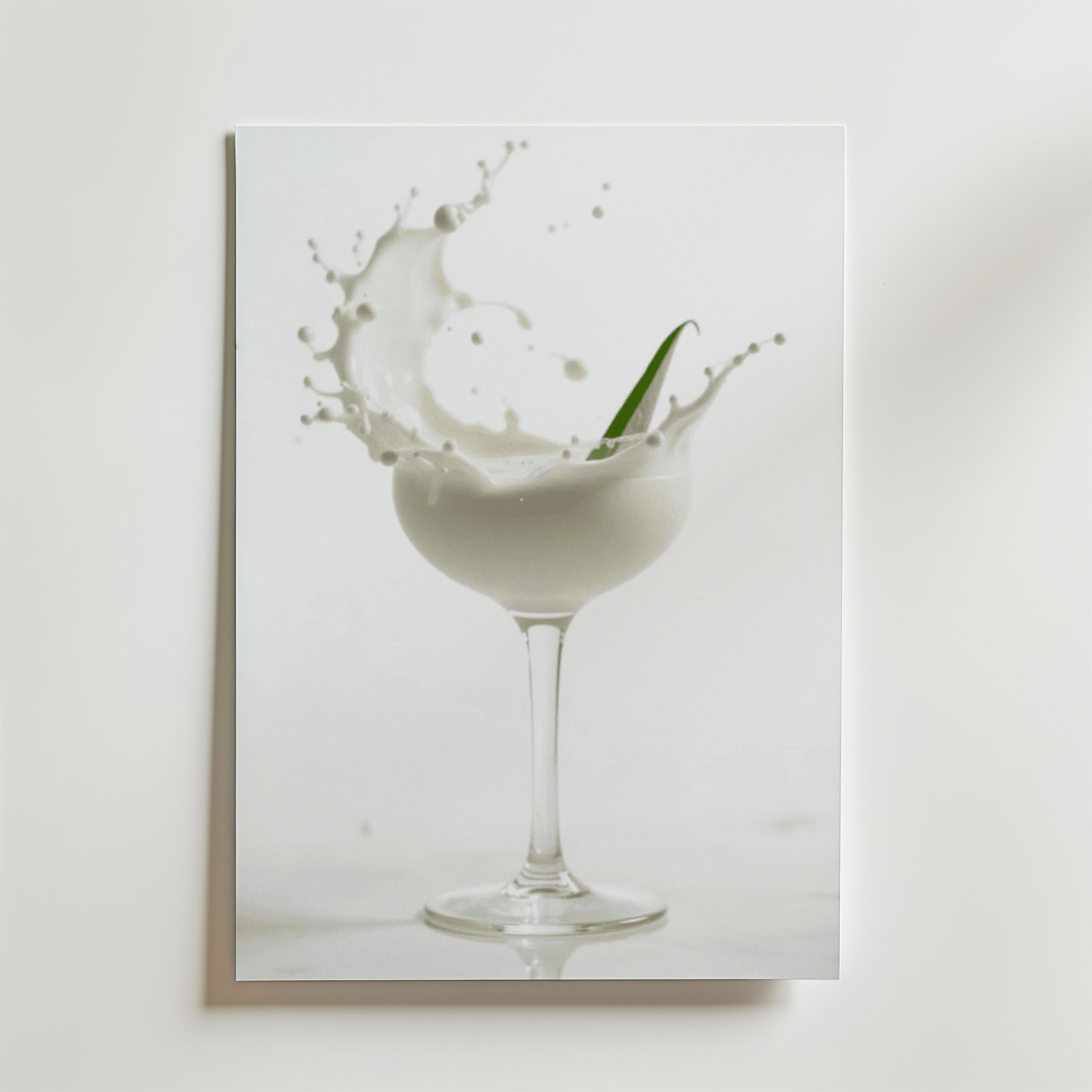 En skvätt mjölk sprutar ur en glasbägare med ett grönt blad hängande i luften, på en vit bakgrund - en elegant Bozetto Foam Champagne Drink Poster, tryckt på premiumpapper med lyxigt matt yta.