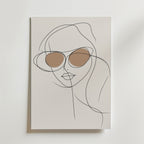 Minimalistisk linjeteckning av en kvinna med runda solglasögon, accentuerad med brun linsskuggning på en ljus bakgrund. Stylish Sunglasses Line Woman Poster från Bozetto är en perfekt modern inredningsdetalj för alla rum.