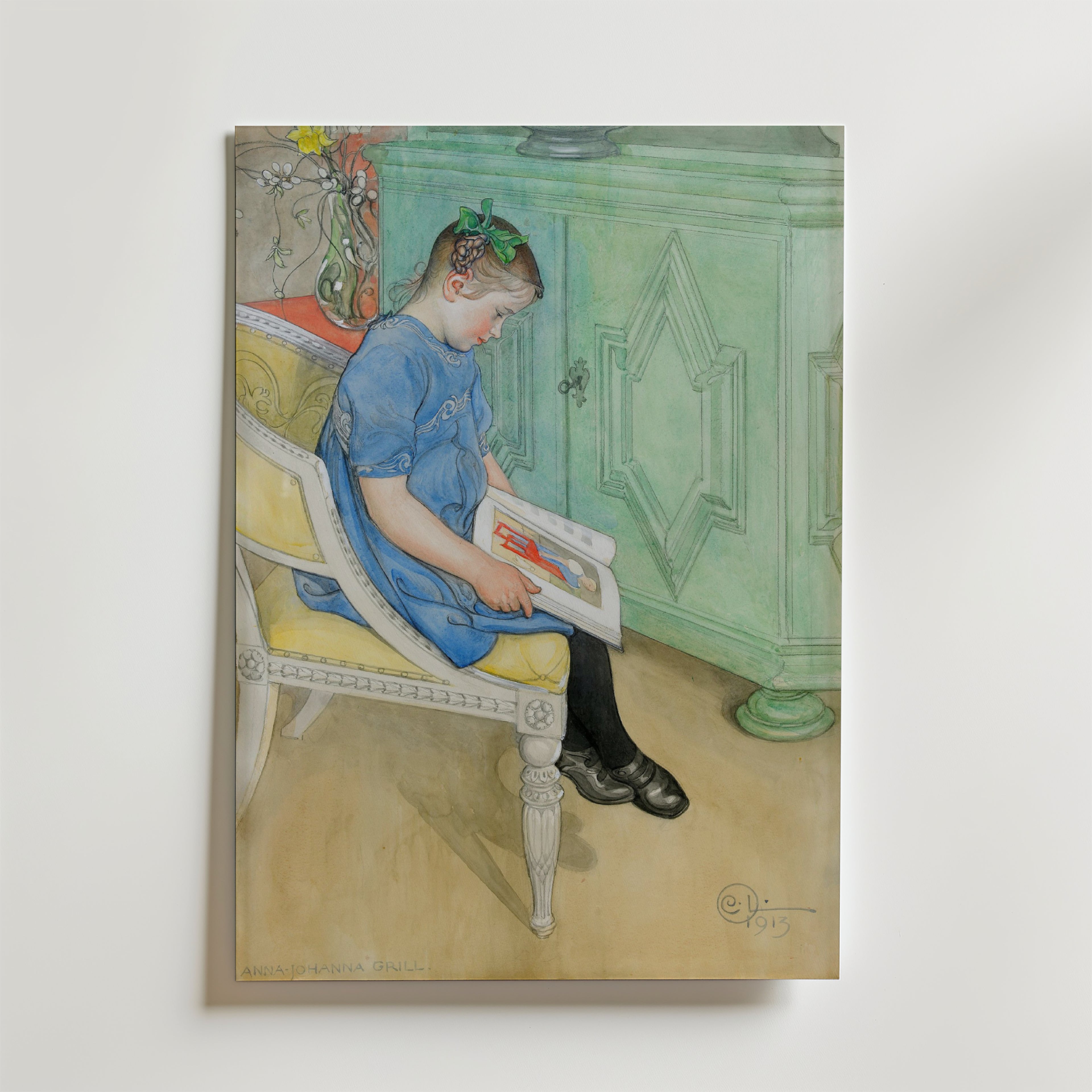 En ung flicka i blå klänning med grön rosett läser en bok på en vit stol. På Carl Larsson Anna Johanna Poster by Bozetto är hon placerad i en pastellgrön inredning med ett grönt skåp och en vas med blommor i bakgrunden.