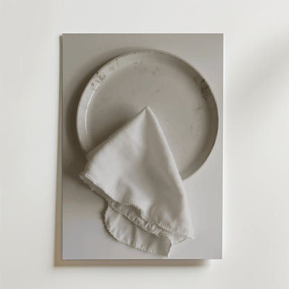 En Bozetto White linen dinner napkin Poster visar en vit keramiktallrik som toppas med en fransig vit linneservett, allt mot en vit bakgrund med en lyxig matt finish.