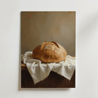 Sourdough Bread Loaf Poster by Bozetto visar ett rustikt bröd på ett träbord med en vit duk, mjukt upplyst mot en neutral bakgrund - tryckt på premiumpapper för en elegant finish.