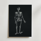 Dancing Skeleton Poster från Bozetto visar ett vitt anatomiskt skelett på en svart bakgrund, vilket skapar slående svartvit konst mot en vanlig vit vägg.