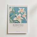 Bozetto Hokusai Lily Poster visar vita liljor med gröna blad och rosa toppade kronblad på en blå bakgrund. Text nedan: HOKUSAI HORTENSIA OCH SVALA 1833-1834 TOKYO JAPAN.