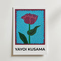 Yayoi Kusama Flower Pulse Poster by Bozetto har en stiliserad röd blomma med gröna blad på en blåmönstrad bakgrund, röd punktkant och fet "YAYOI KUSAMA" text på FSC-certifierat premiumpapper.