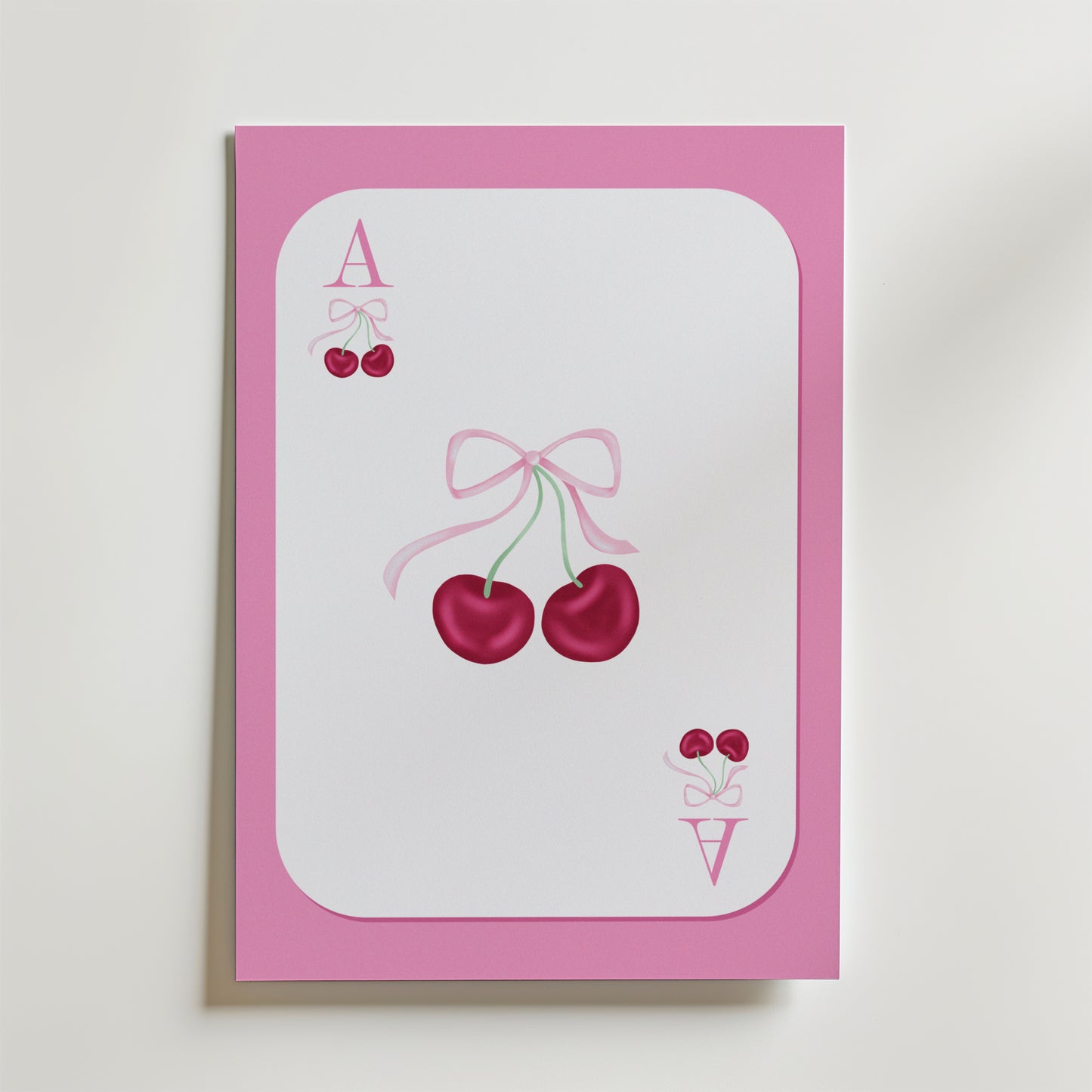 Ace of Cherries Poster by Bozetto föreställer ett spelkort med en rosa kant, två körsbär i mitten som är bundna med ett rosa band och små körsbär bredvid bokstäverna A och V i hörnen.