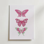 Postern Pink Butterfly Trio Poster från Bozetto föreställer tre illustrerade fjärilar i rosa och mintgrönt staplade vertikalt på en vit bakgrund, vilket framhäver deras unika vingmönster och eleganta skönhet.